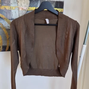 Brun bolerotopp - Säljer en stilren brun bolerotopp med långa ärmar. Toppen har en ribbad kant och är perfekt för lager-på-lager-stil. Passar bra till både vardag och speciella tillfällen.