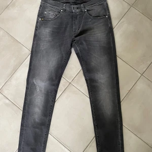 Grå jeans från Tiger of Sweden - Snygga grå jeans från Tiger of Sweden med en modern tvätt och slitna detaljer på benen. De har en klassisk femficksdesign och knappgylf. Perfekta för en stilren look.