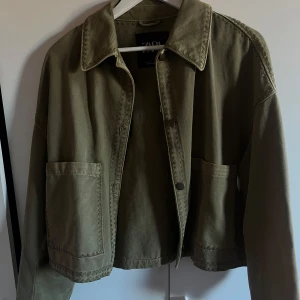 Olivgrön jacka från Zara - Säljer en olivgrön jacka från Zara med en avslappnad passform. Jackan har stora fickor framtill och en klassisk krage. Perfekt för en stilren look. Bara använd några få gånger, jackan är ljusare grön i verkligheten! 