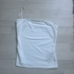 Vit axelbandslös tubtopp - Säljer en stilren vit tubtopp. Perfekt för varma sommardagar eller som ett basplagg i garderoben. Enkel och snygg design som passar till det mesta.