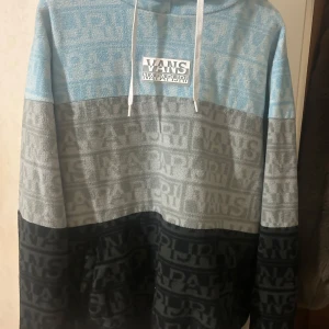 Flerfärgad hoodie från Vans x Napapijri - Säljer en cool flerfärgad hoodie från Vans x Napapijri. Tröjan har ett blockmönster i blått, grått och svart med logotypdetaljer över hela. Den har en justerbar huva med vita snören och är perfekt för en avslappnad stil.