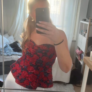 Blommig korsettopp - Säljer en snygg korsettopp med ett blommigt mönster i rött och blått. Toppen är axelbandslös och har en tight passform som framhäver figuren. Perfekt för en kväll ute eller en speciell tillställning. 