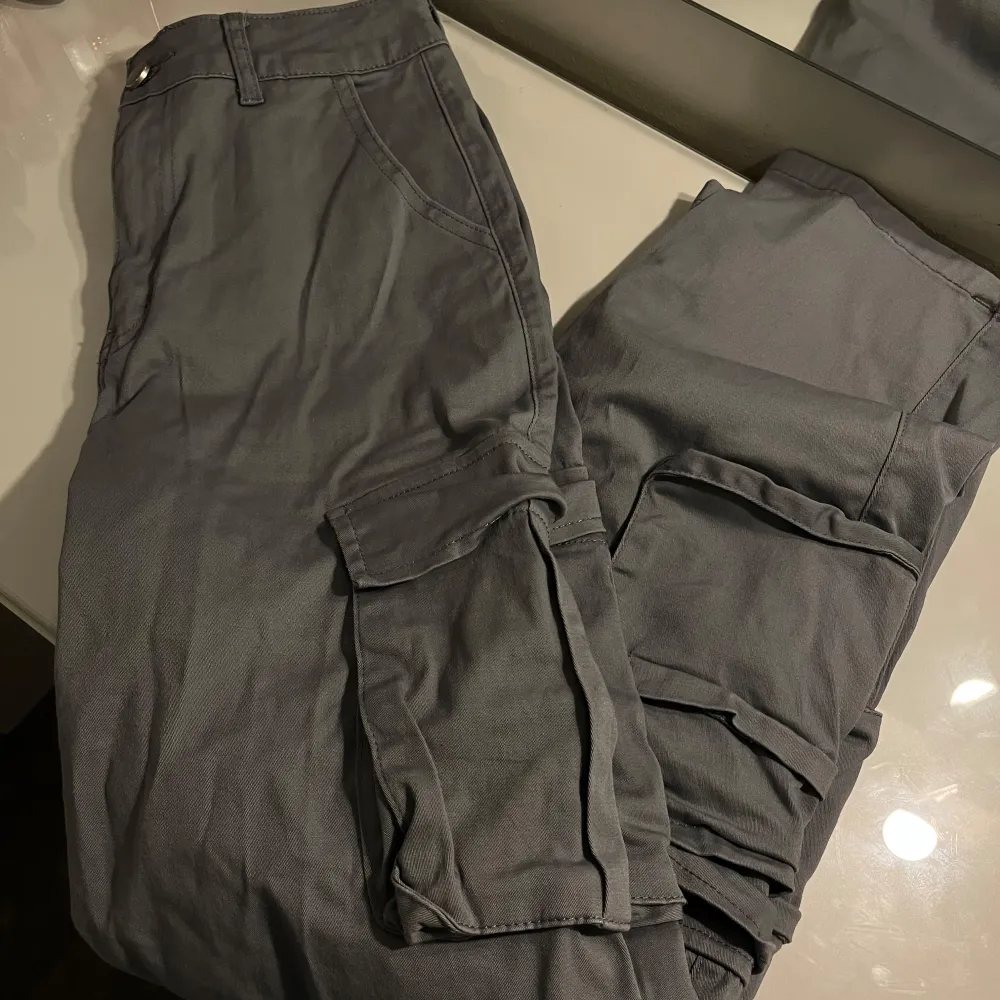 Säljer ett par grå cargopants med flera praktiska fickor. Byxorna har en avslappnad passform och är perfekta för en casual look. De är tillverkade i ett slitstarkt material och har en klassisk design med knapp och dragkedja🤍. Farkut & Housut.