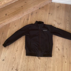 Svart jacka från Peak Performance - Säljer en stilren svart jacka från Peak Performance. Jackan har en dragkedja framtill och ribbade muddar vid ärmslut och nederkant. Perfekt för kyligare dagar med sina långa ärmar och bekväma passform.Har inget håll
