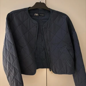 Blå quiltad jacka från Zara - Säljer en snygg blå quiltad jacka från Zara. Jackan har en croppad design med långa ärmar och en dragkedja framtill. Perfekt för en stilren look. Nästan i nyskick! Endast använd en gång🥰🥰