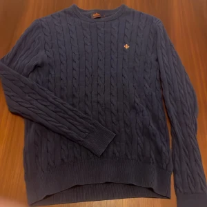 Mörkblå stickad tröja från Morris - Säljer en stilren mörkblå stickad tröja från Morris med kabelstickat mönster. Tröjan har långa ärmar och en liten broderad detalj på bröstet. Perfekt till användning vid finare tillfällen och även till en avslappnad look. Storlek M passar även S. Skick är 9/10 det är inga defekter på den!