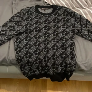 Svart och grå tröja från Michael Kors - Säljer en snygg svart och grå tröja från Michael Kors med ett diagonalt mönster av logotypen. Tröjan har långa ärmar och ribbade muddar vid armslut och vid nederkant, säljer på grund av att jag inte passar i den längre. Michael kors loggan har lossnat men går att sy tillbaks. Skriv för mer frågor och bilder 👍