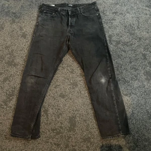 Svarta jeansbyxor Jack and Jones - Säljer ett par svarta jeansbyxor med en loose passform. Byxorna har en klassisk femficksdesign och är perfekta för en avslappnad stil. De har en knappgylf och är tillverkade i ett slitstarkt material.