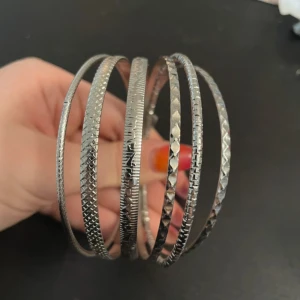 Set med silverfärgade armband - Snyggt set med flera silverfärgade armband i olika mönster. Perfekt för att lägga till en glittrig touch till din outfit. Armbanden har en elegant och stilren design som passar till många tillfällen.