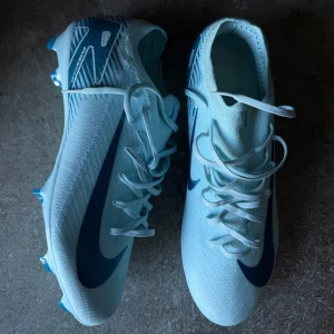 Nike fotbollsskor i ljusblått - Snygga ljusblå Nike fotbollsskor med mörkblå detaljer och snörning. Perfekta för fotbollsplanen med en stilren design och bra grepp.