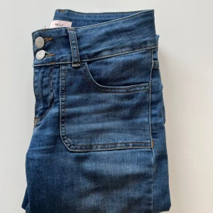 Blå jeans från Nelly - Knappt använda jeans från Nelly med låg midja och två knappar där fram. Även knappar på fickorna där bak