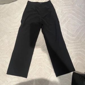 Svarta kostymbyxor från 157 - Snygga svarta kostymbyxor från 157 med hög midja och rak passform. Perfekta för en stilren look. Byxorna har en klassisk design med dragkedja och knapp framtill. Inköpta i december som julklapp men glömde returnera dem