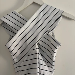 Randig topp från Zara - Snygg ärmlös topp med svartvita ränder. Perfekt för en stilren look. Klänningen har en unik krage som ger en modern touch.