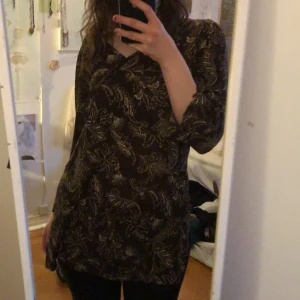 Mönstrad blus från Lindex - Säljer en snygg mönstrad blus från Lindex i mörka toner med ett elegant blommönster. Blusen har trekvartsärmar som ger en stilren look. Perfekt för att piffa upp garderoben!