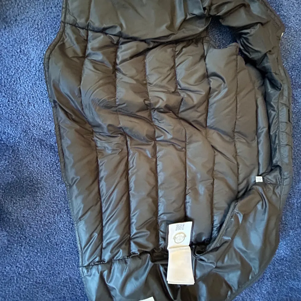 Snygg svart dunväst från Moncler med dragkedja och två fickor med dragkedjor. Perfekt för kyligare dagar och ger en stilren look. Moncler-loggan pryder bröstet för en exklusiv touch.. Takit.