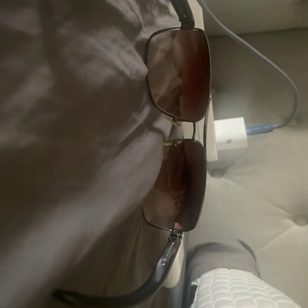 Snygga solglasögon från Prada med bruna glas och en elegant metallram. Skalmarna har en röd detalj med Prada-loggan. Perfekta för en stilren look.. Asusteet.