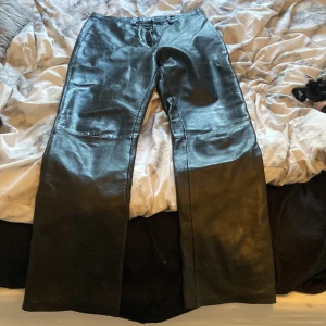 Svarta skinnbyxor från Saki - Snygga svarta skinnbyxor från Saki med en klassisk design. Byxorna har en rak passform och är tillverkade i äkta skinn, vilket ger en stilren och tidlös look. Perfekta för att ge din outfit en edgy touch.