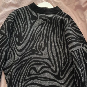 Svart och silver glittrig tröja från & Other Stories - Säljer en snygg svart tröja från & Other Stories med ett glittrigt zebramönster i silver. Tröjan har långa ärmar och en ribbad krage. Perfekt för att sticka ut med stil! 🖤✨