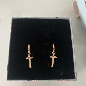Guldörhängen med korsdesign - Snygga guldörhängen med korsdesign, dekorerade med små glittrande stenar. Perfekta för att ge en elegant touch till din stil. ROSTAR INTE! 