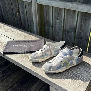Camouflage sneakers från Philippe Model - Snygga sneakers från Philippe Model i en cool grå och blå camouflage-design. Skorna har snörning och en kontrasterande svart häl. Perfekta för en stilren och avslappnad look. Dustbagen inngår! Passar till dig som har 42-43. Skicket är 8/10, använda några få gånger. Hör av dig vid minsta fråga👍🏼 (kan också tänka mig byta mot några andra skor i stl 44)