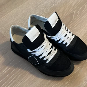 Svarta sneakers från Philippe Model - Snygga svarta sneakers från Philippe Model med vita detaljer och snörning. På vänster skorn har tyget gått lite sönder. Men går fortfarande utmärkt att använda.
