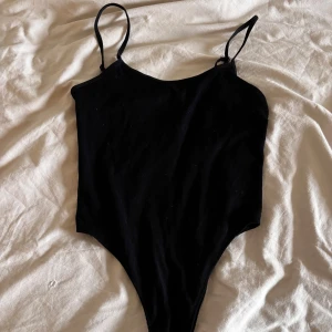 Svart ribbad body från Zara - Säljer en stilren svart body från Zara med smala axelband och ribbad textur. Perfekt för att matcha med jeans eller kjol. Den har praktiska knappar i grenen för enkel på- och avtagning.😍