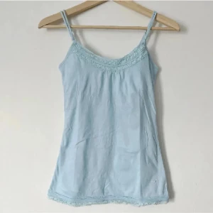 Y2k Ljusblå linnetopp med spetsdetaljer - Säljer en söt ljusblå linnetopp med smala axelband och spetsdetaljer vid halsringning och nederkant. Perfekt för varma sommardagar eller som ett lager under en tröja. Storlek M (S).