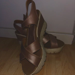 Lila/rosa sandaler med kilklack - Snygga bruna sandaler med kilklack och korsade remmar. De har en öppen tå och justerbar rem runt ankeln för bättre passform. Perfekta för sommarens alla tillfällen. Lite smutsiga men inget jag inte kan få bort med våtservetter!