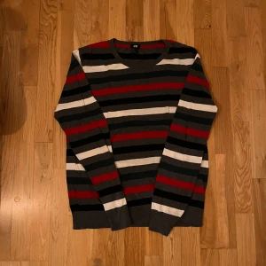 Randig tröja från H&M - Säljer en randig tröja från H&M i färgerna svart, grå, röd och vit. Tröjan har långa ärmar och en klassisk rund halsringning. Perfekt för en avslappnad stil.