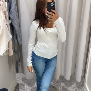 Vit långärmad topp - Säljer en stilren vit långärmad topp med fyrkantig halsringning. Toppen har en tight passform och är perfekt för lager-på-lager eller att bära som den är. Den är både bekväm och mångsidig.