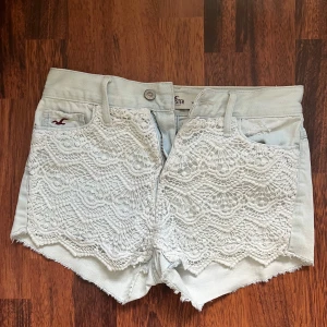 Vita spetsdetaljerade shorts från Hollister - Snygga vita shorts från Hollister med spetsdetaljer på framsidan och fransiga kanter. De har en knapp och dragkedja framtill samt två bakfickor med dekorativa sömmar. Perfekta för en somrig look! Använda endast 2-3 ggr och säljs för att dem är för små. Pris kan diskuteras! 