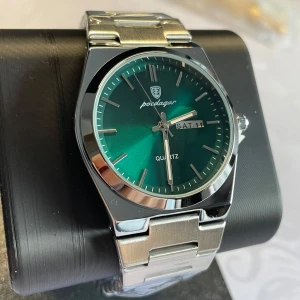 Grön Hugo Poedagar Klocka - Helt ny oanvänd snygg klocka från Hugo Poedagar med grön urtavla och dagvisning. Länkborttagare medföljes ✅ Armbandet är i silverfärgat metall och klockan har en kvartsrörelse. Perfekt för den som vill ha en stilren accessoar. 40mm 