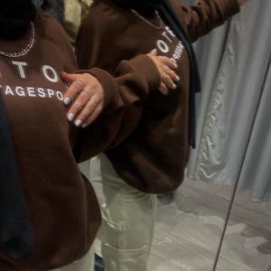 Brun sweatshirt med tryck - Säljer en brun sweatshirt med tryck framtill. Tröjan har långa ärmar och en avslappnad passform, perfekt för en casual look. Den är mjuk och bekväm, idealisk för kyligare dagar.