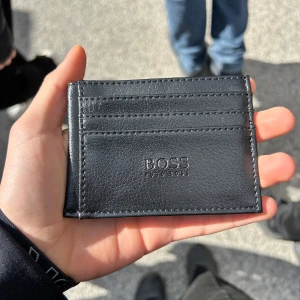 Svart plånbok från Boss - Säljer en svart plånbok från boss. Den ör helt ny aldrig använd och alla som har sett den haf tyckt den va skit snygg. Kan hålla många kort och cash. Pris kan diskuteras, om du köper Kepsen och plånboken samtidigt får du båda för 300