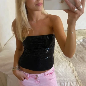 Fest topp  - Säljer en snygg svart tubtopp med glittrande paljetter. Perfekt för en kväll ute eller festliga tillfällen. Toppen är ärmlös och har en tight passform som framhäver figuren. Ett måste för garderoben!