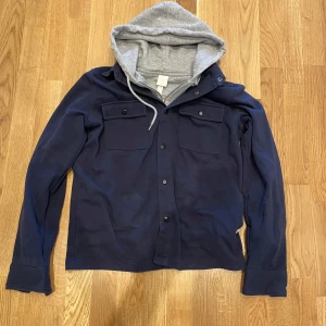 Mörkblå overshirt - Säljer en stilren mörkblå overshirt. Jackan har långa ärmar och knappar framtill samt två bröstfickor med lock. Perfekt för en avslappnad look.