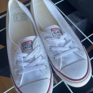 Vita Converse All Star sneakers - Säljer ett par klassiska vitaConverse CHUCK TAYLOR ALL STAR BALLET LACE.  Skorna har den ikoniska röda och blå randen runt sulan och är perfekta för en avslappnad stil.  Ballerinamodell. 