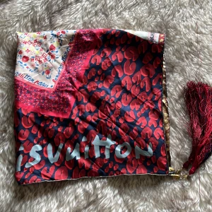 Mönstrad scarf från Louis Vuitton - Snygg och färgglad scarf från Louis Vuitton med leopardmönster i rött och svart, samt inslag av blommiga och randiga detaljer. Den har en dekorativ tofs i ena hörnet och är tillverkad i siden. Perfekt för att ge din outfit en lyxig touch!