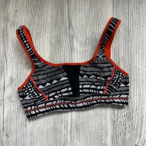 Mönstrad sporttopp från Björn Borg small - Snygg sporttopp från Björn Borg med svartvitt mönster och orange detaljer. Toppen har breda axelband och en bekväm passform, perfekt för träning. Den har en unik design med olika geometriska mönster och en justerbar knäppning bak. Storlek Small