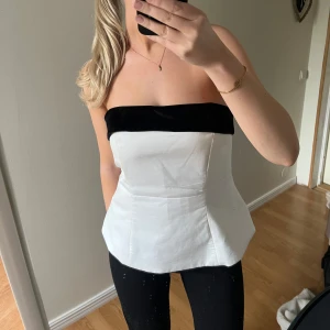 Vit och svart tubtopp - Snygg vit tubtopp med svart detalj upptill samt rosett på baksidan. Den har legat vikt därav är den skynklig, men går att stryka bort. Nypris: 450