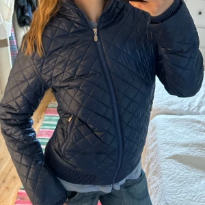 Blå quiltad jacka - Snygg blå quiltad jacka med dragkedja och ribbade muddar. Jackan har en stilren design med långa ärmar och en hög krage. 