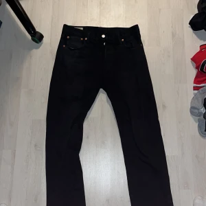 Svarta Levis 501 jeans - Säljer ett par klassiska svarta Levis 501 jeans. De har en rak passform och är tillverkade i slitstarkt denim. Byxorna har fem fickor och knappar i gylfen. Perfekta för en stilren look.
