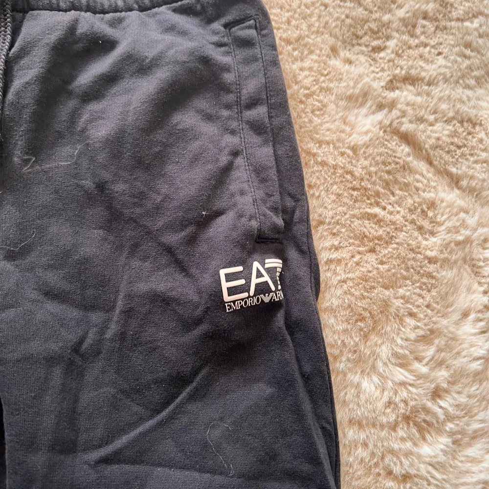 Snygga svarta mjukisbyxor från Emporio Armani med elastisk midja och EA7-logga på sidan. Perfekta för en avslappnad stil med bekväm passform.. Farkut & Housut.