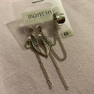 Silverfärgade örhängen med kedjor och vingar  - Snygga silverfärgade örhängen med kedjor och dekorativa vingar. Örhängena har även små pärldetaljer som ger en extra touch. Perfekta för att ge din outfit en unik stil.