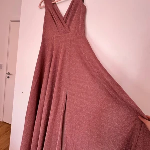 Glittrig rosa långklänning från bubbleroom, helt ny storlek M - Säljer en fantastisk glittrig rosa långklänning från bubbleroom. Klänningen har en v-ringad design och en elegant slits framtill. Perfekt för speciella tillfällen!