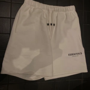 Vita shorts från Essentials Fear of God - Säljer ett par stilrena vita shorts från Essentials Fear of God. De har en bekväm elastisk midja med snörning och en diskret logga på benet. Perfekta för en avslappnad look.