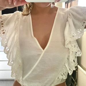 Vit omlottblus med spetsdetaljer - Säljer en söt vit omlottblus med v-ringning och vackra spetsdetaljer på ärmarna. 