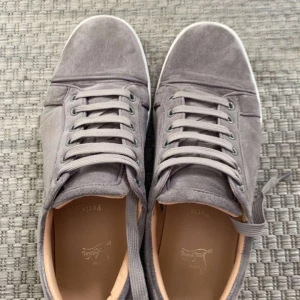 Grå sneakers med snörning - Snygga grå sneakers i mocka med klassisk snörning och rund tå. Skorna har en unik röd sula med mönster, vilket ger dem en exklusiv touch. Perfekta för en stilren look.