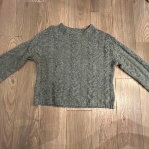Grå stickad tröja från 157 - Säljer en mysig grå stickad tröja från 157. Tröjan har ett klassiskt flätmönster och långa ärmar. Perfekt för kyliga dagar. Passar bra till både jeans och kjol. Pris kan diskuteras