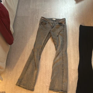 Grå bootcut jeans från Gina Tricot - Snygga grå bootcut jeans från Gina Tricot med klassisk femficksdesign och knappar. Perfekta för en stilren look med en touch av retro. Passar bra till både sneakers och klackar.